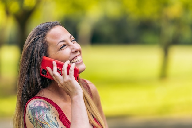 Mulher com roupas de verão, falando em seu telefone celular enquanto sorria em um parque.