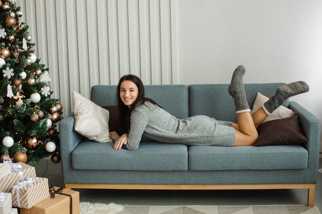 Mulher com roupas quentes relaxando perto da árvore de Natal