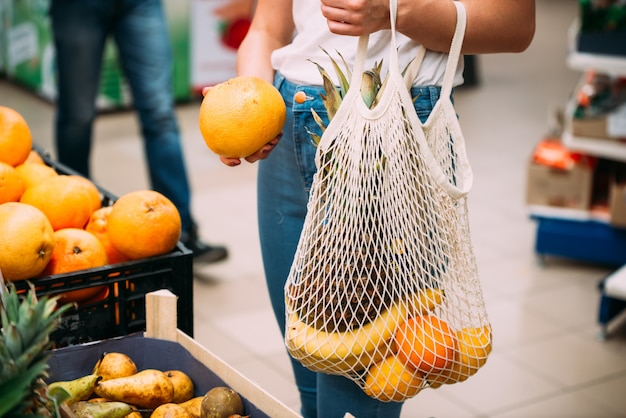 Mulher com saco de malha cheia de legumes frescos, compras na loja, conceito zero de resíduos