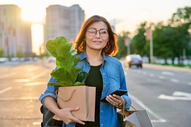 Mulher com sacolas de papel de compras comprou planta andando ao ar livre