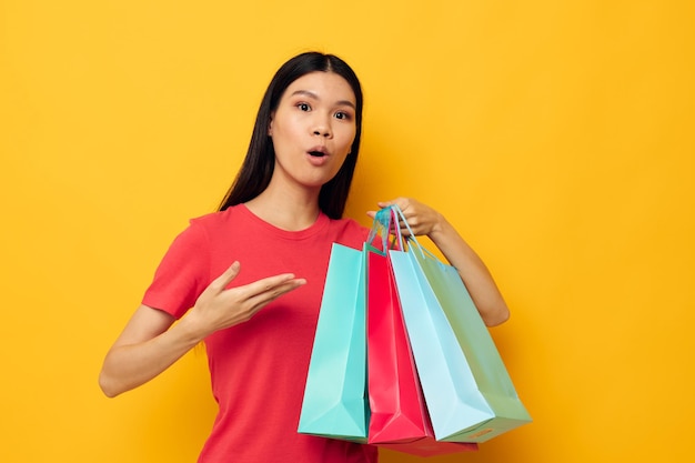 Mulher com sacos de compras de aparência asiática em fundo isolado de camiseta vermelha inalterado