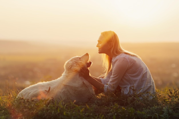 Foto mulher com seu cachorro brincando na colina ao pôr do sol