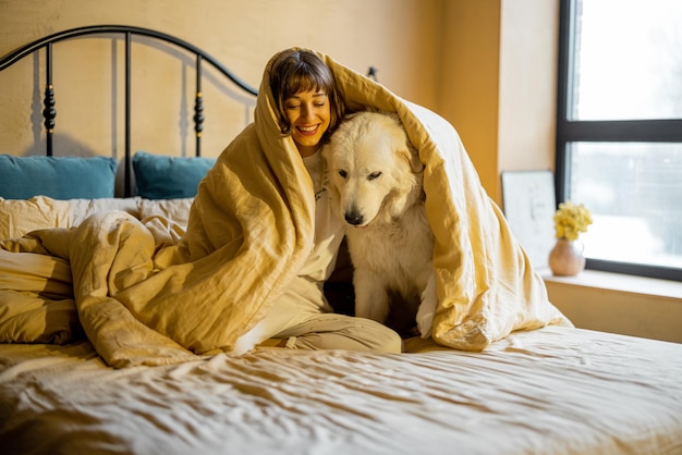 Mulher com seu cachorro debaixo do cobertor na cama