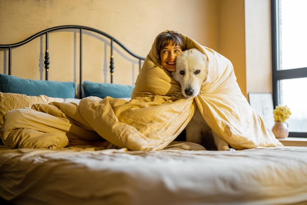 Mulher com seu cachorro debaixo do cobertor na cama