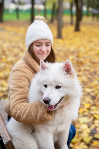 Mulher com seu cachorro no outono em um parque. Mulher está abraçando-o no banco, sorrindo.