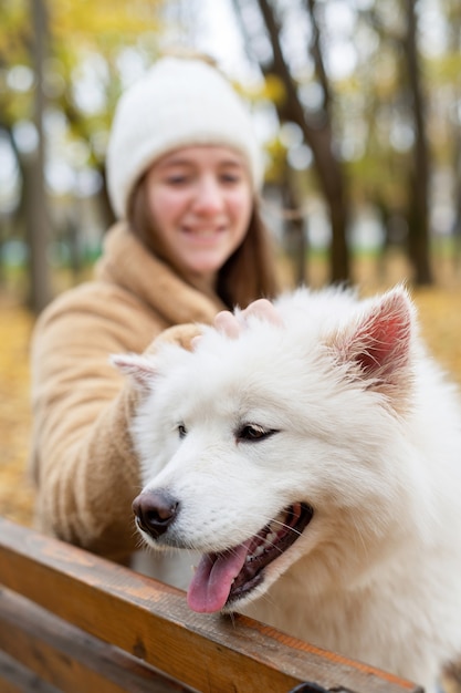 Mulher com seu cachorro no outono em um parque. Mulher está acariciando-o no banco, sorrindo.