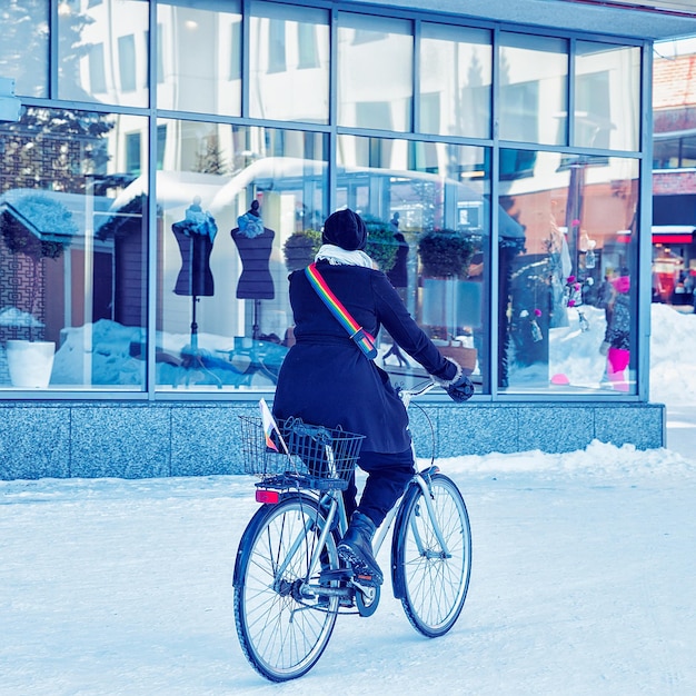 Mulher com sinal de arco-íris LGBT andando de bicicleta na rua nevada do inverno Rovaniemi, Lapônia, Finlândia.