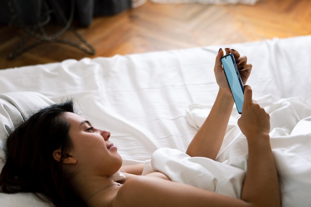 Mulher com smartphone na cama com lençóis brancos