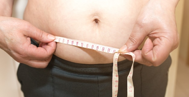 Mulher com sobrepeso está medindo sua cintura. Barriga gorda com centímetro com fita métrica.