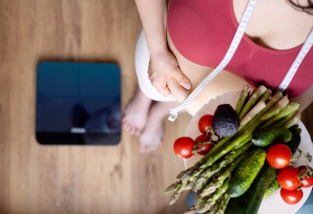 Foto mulher com sobrepeso na cozinha com centímetro de fita métrica na cintura segurando a gordura da barriga com handfemale