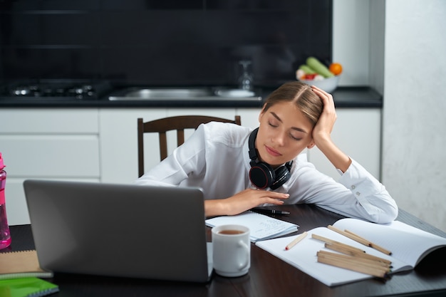 Mulher com sono sentada à mesa com o laptop aberto