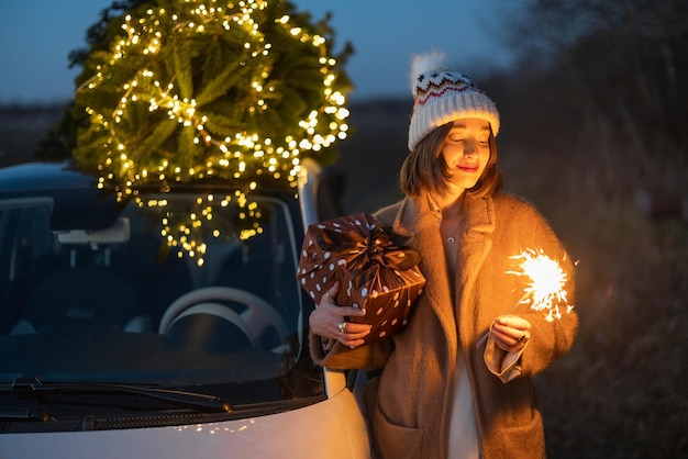 Mulher com sprklers perto do carro e árvore de Natal ao ar livre