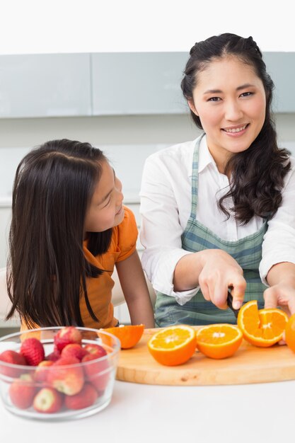 Mulher com sua filha nova cortando frutas na cozinha