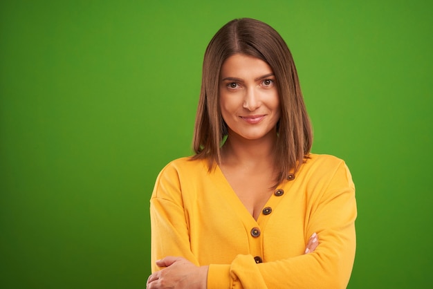 Foto mulher com suéter amarelo olhando para a câmera sobre fundo verde