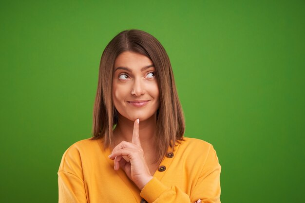 mulher com suéter amarelo pensando e apontando sobre um fundo verde