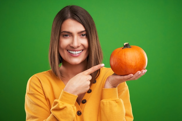 mulher com suéter amarelo segurando abóbora sobre fundo verde