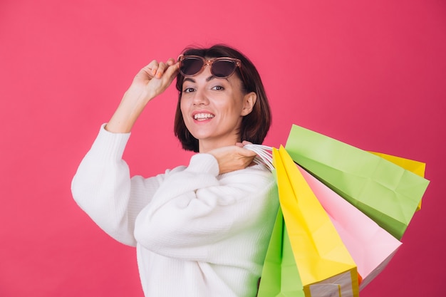 Mulher com suéter branco casual e óculos escuros na parede vermelha