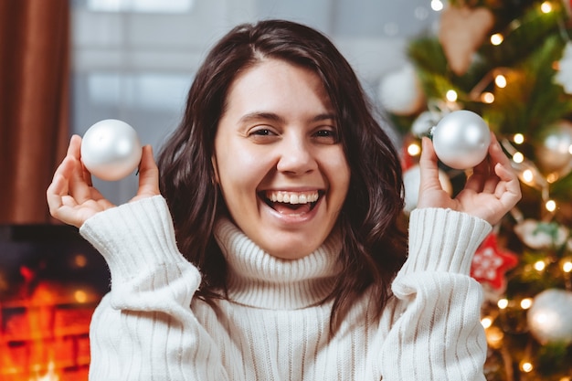 mulher com suéter branco posando perto do retrato da árvore de natal