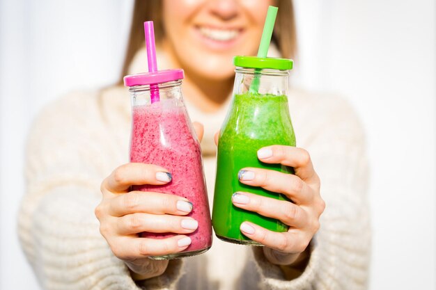 Mulher com suéter de lã com 2 garrafas de suco fresco rosa e verde