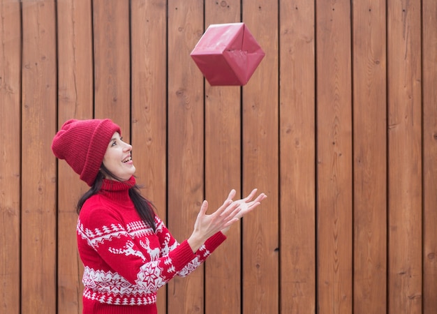 Mulher com suéter de Natal pegando um presente de Natal voador na parede de madeira