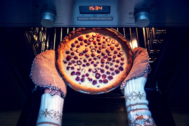 Mulher com suéter de Natal tira o bolo de framboesa do forno.