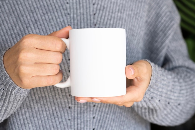 Mulher com suéter quente segurando uma caneca branca nas mãos maquete de copo de inverno para presentes individuais de natal