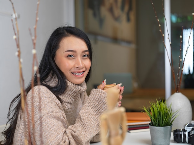 Mulher com suéter segurando uma xícara de café com leite quente