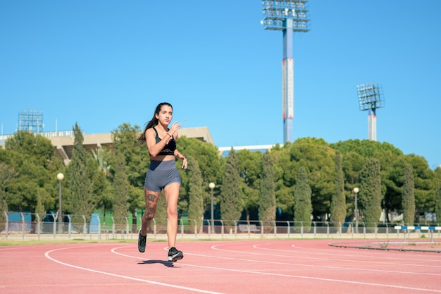 Mulher com tatuagens correndo na pista de atletismo em um dia ensolarado