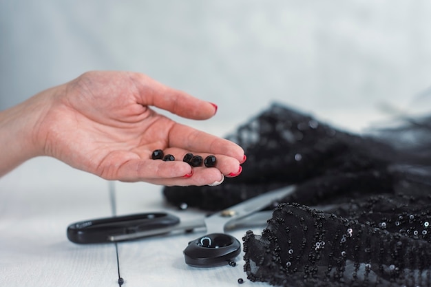 Mulher com tecido de cetim preto com tesoura em um fundo de madeira com miçangas.