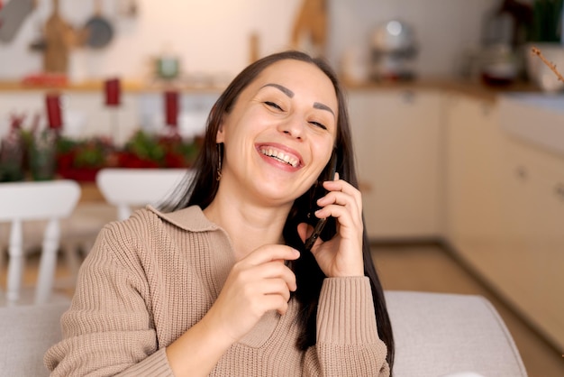 Mulher com telefone nas mãos sentada em casa na cozinha no sofá durante as férias de Natal