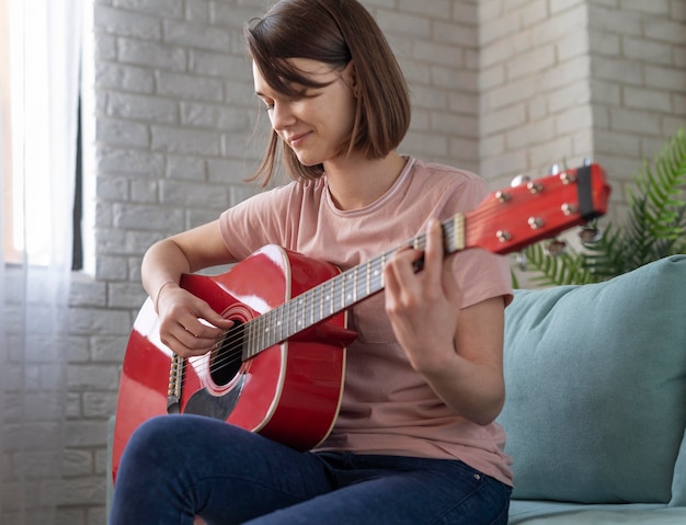 Mulher com tiro médio tocando guitarra no sofá
