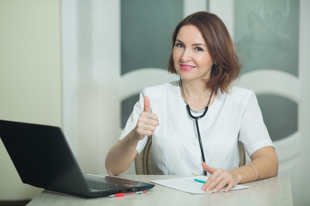 mulher com túnica branca na mesa com laptop e gesto de mão