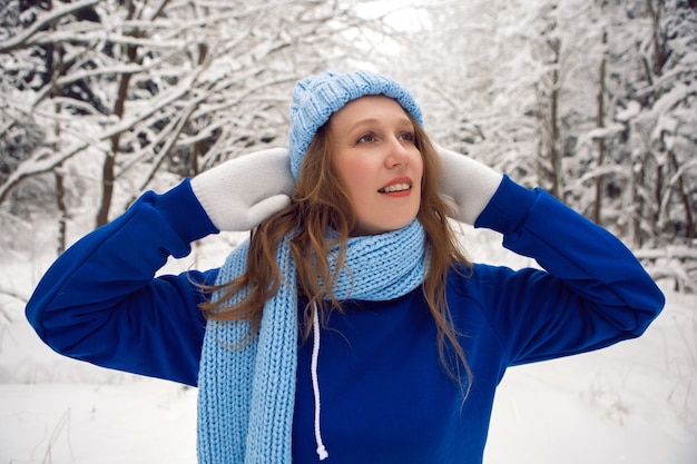 Mulher com um agasalho esportivo azul, luvas brancas e lenço fica no inverno em uma floresta coberta de neve