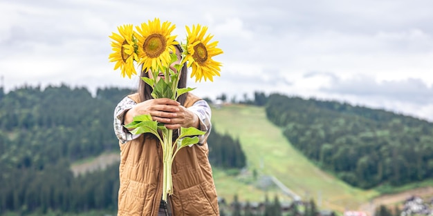 Mulher com um buquê de girassóis na natureza em uma área montanhosa