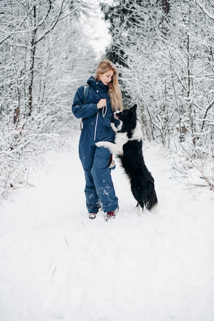 Mulher com um cachorro border collie preto e branco na floresta de neve