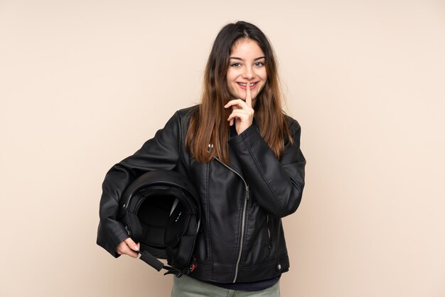 Mulher com um capacete de moto isolado na parede bege, fazendo o gesto de silêncio