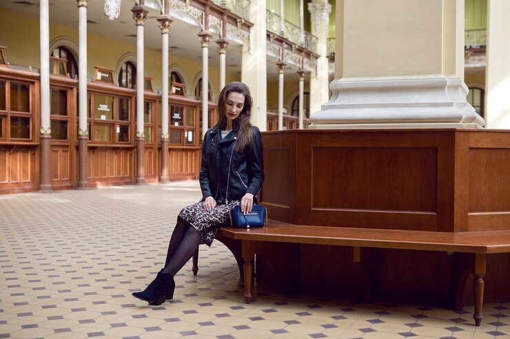 Foto mulher com um casaco de couro preto e uma bolsa azul sentada na biblioteca