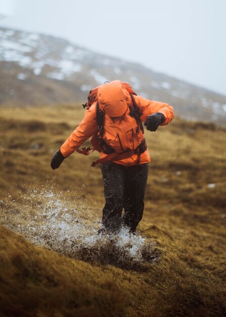 Mulher com um casaco laranja caminhando sob a chuva nas ilhas faroe