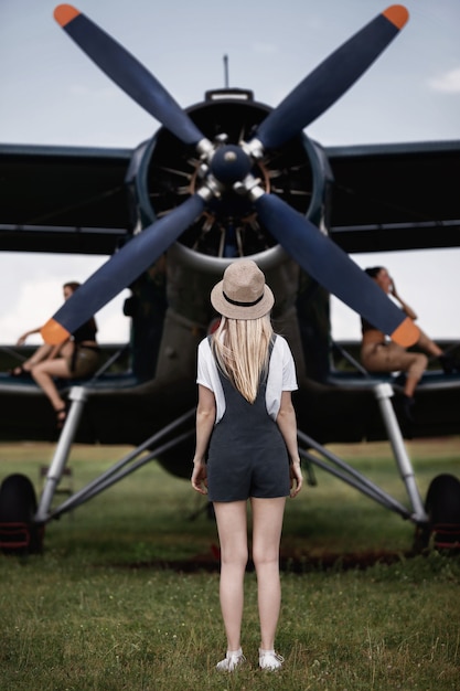 Mulher com um chapéu de palha no fundo, posando no cenário de um avião com uma hélice