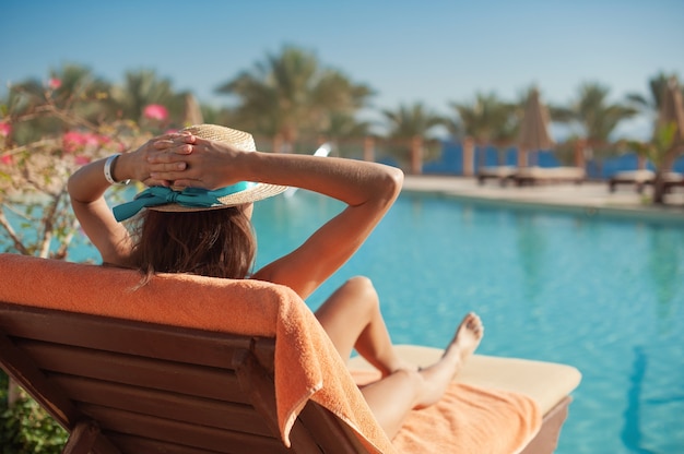 Mulher com um chapéu de palha relaxando perto de uma luxuosa piscina de verão