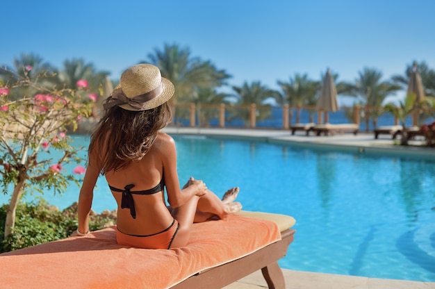 Mulher com um chapéu de palha relaxante em um sofá perto de um luxuoso hotel de piscina de verão Egito, conceito de tempo para viajar