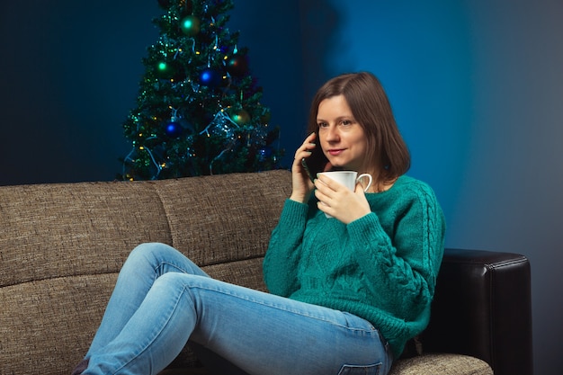 Mulher com um copo de bebida quente no ônibus falando ao telefone com parentes comemorando o natal