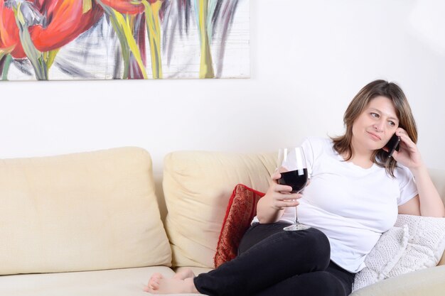 Mulher com um copo de vinho e falando no telefone.