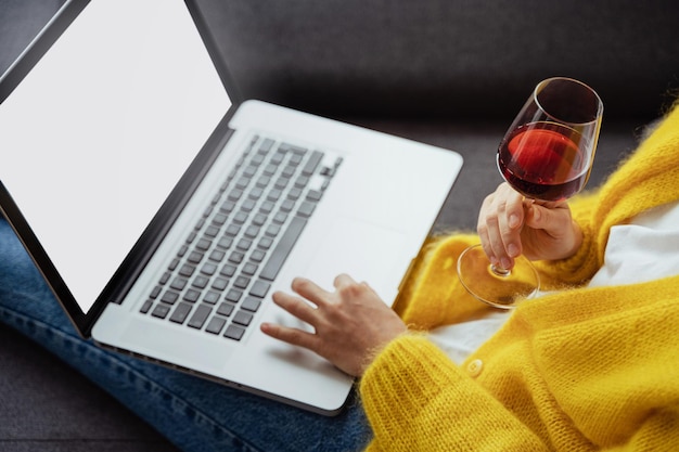 Mulher com um copo de vinho tinto está usando laptop em casa