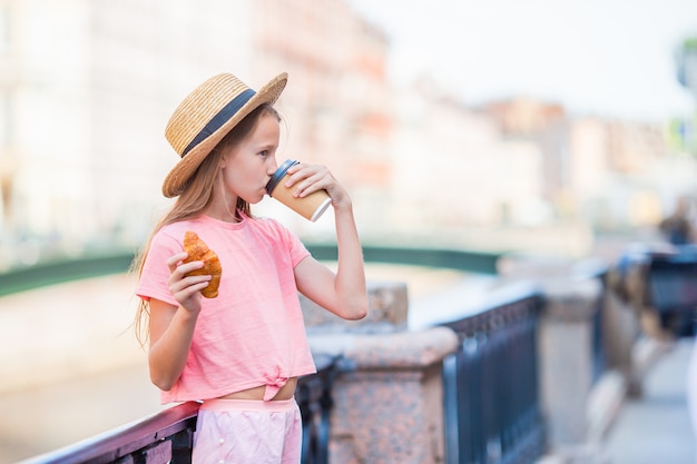 Mulher com um croissant e café ao ar livre no passeio