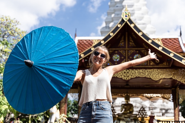 mulher com um guarda-chuva em uma mão com os braços abertos na frente de um templo budista