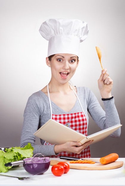 Mulher com um livro de receitas e uma colher de pau na cozinha