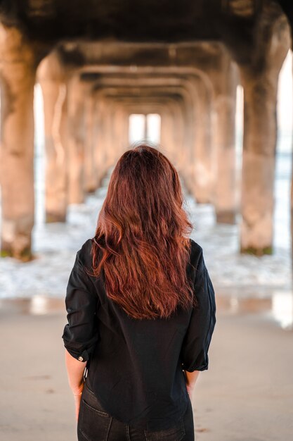 Mulher com um paletó caminha sob o píer em Manhattan Beach, em Los Angeles, Califórnia