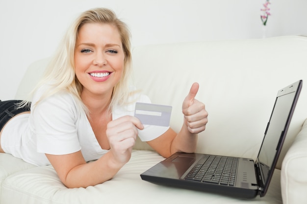 Mulher com um polegar para cima e um cartão de crédito usando um laptop