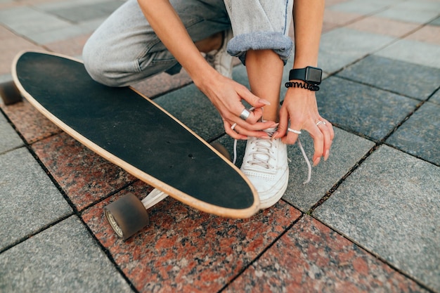 Mulher com um skate está amarrando seus tênis em um pavimento de concreto